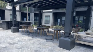 Un patio al aire libre con varias mesas y sillas, una parrilla y un espacio de descanso con cojines.
