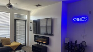 Una sala de estar moderna con chimenea, televisor de pantalla plana y un letrero de neón que dice 