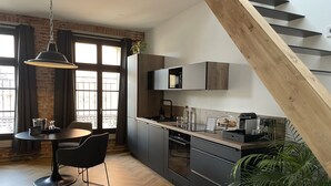 A modern kitchen with dark cabinetry, a wooden dining table, and a black chair. - Ennéa - Jacuzzi & Luxury Suites (Perpignan)
