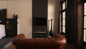 A modern hotel room with a leather sofa, a flat-screen TV, and a large window. - Ennéa - Jacuzzi & Luxury Suites (Perpignan)