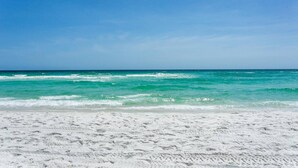 Una playa de arena blanca y olas oceánicas turquesa bajo un cielo azul despejado.