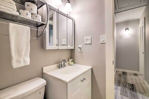 A bathroom with a toilet, sink, and mirror. There are towels and toilet paper on a shelf. - Bright Jonestown Retreat w/ Yard & Porch! (Jonestown)