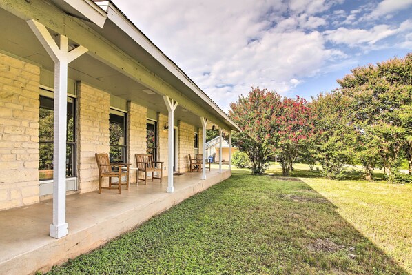 A covered outdoor area with a brick building, wooden chairs, and a well-maintained lawn. - Bright Jonestown Retreat w/ Yard & Porch! (Jonestown)