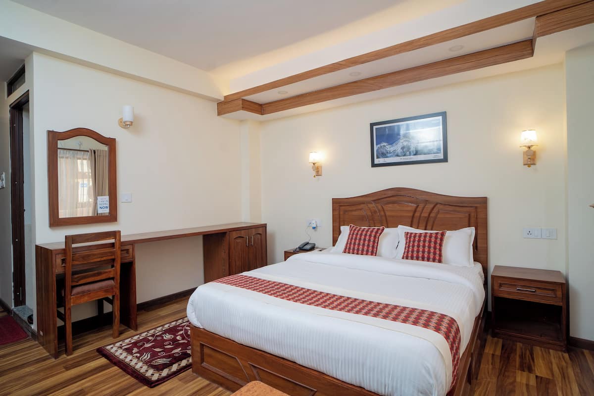 A bedroom with a wooden bed, bedside tables, a desk, and a chair.