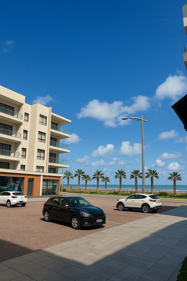 Un edificio moderno con varios balcones, un estacionamiento con coches y un cielo azul despejado.