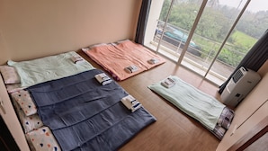 A room with three beds, each with a different colored bedspread and pillows, and a large window with a view of greenery and a building outside. - YYK Hostel 24 (Nakhon Chai Si)