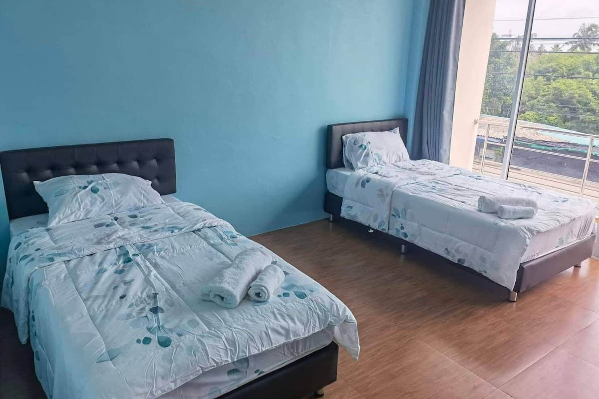 A hotel room with two beds, a large window, and a view of greenery outside.