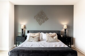 A neatly made bed with a grey headboard, two bedside tables with lamps, and a decorative wall piece. - Diamond Retreat Townhome, Garage, 3 mi to Downtown (Nashville)