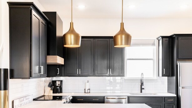 A modern kitchen with dark cabinets, a white countertop, a stainless steel refrigerator, and two pendant lights.