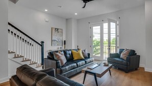 A modern living room with a staircase, leather sofas, a coffee table, and a ceiling fan.
