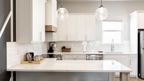 Une cuisine moderne avec des meubles blancs, un îlot central et des luminaires suspendus.