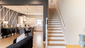 Une cuisine moderne avec des meubles blancs, un coin repas doté d’un canapé noir et un escalier menant à un autre niveau.