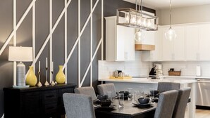 Une cuisine moderne avec des meubles blancs, une table à manger noire et des chaises grises, ainsi qu’un luminaire suspendu.