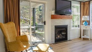 A living room with a fireplace, a television, and a sliding glass door leading to a patio. - Creekside Hideout for Quiet Souls Condo A (Nanoose Bay)