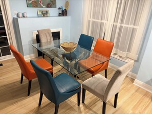 A dining area with a glass table surrounded by chairs, a fireplace, and a window with sheer curtains.