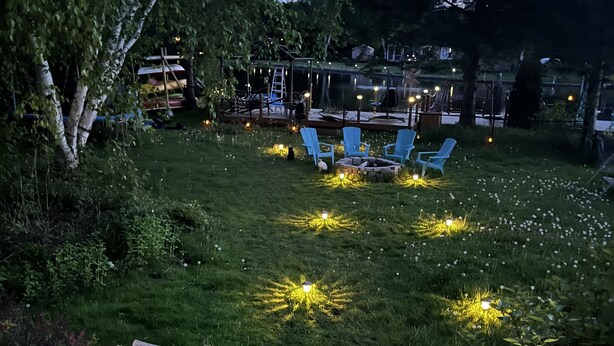 Een terras met houten balustrade en een kleine tuin met gras en een vuurkuil.
