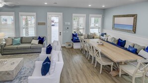 A spacious living area with a sofa, a dining table, and a view of the sea through large windows. - Community Pool/3min to Beach/Screened Patio/2 Lofts/Fire Pit/Foosball&Pingpong/*Golf Cart/Sleeps 16 (Santa Rosa Beach)
