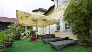 Un espace patio aménagé avec du mobilier d’extérieur, un grand parasol et un jardin bien entretenu.