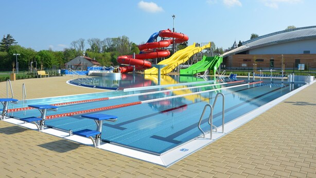 Une piscine avec des couloirs de nage, un toboggan aquatique et une zone couverte pour les spectateurs.