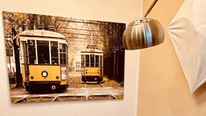 A dining area with a round table, clear chairs, a wall-mounted lamp, and a vintage tram photo.