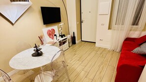 A modern living room with a round table and chairs, a red sofa, a TV mounted on the wall, and a door leading to another room.