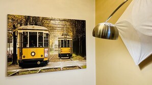 A dining area with a round marble table, a chandelier, a wall-mounted lamp, and a vintage tram poster.