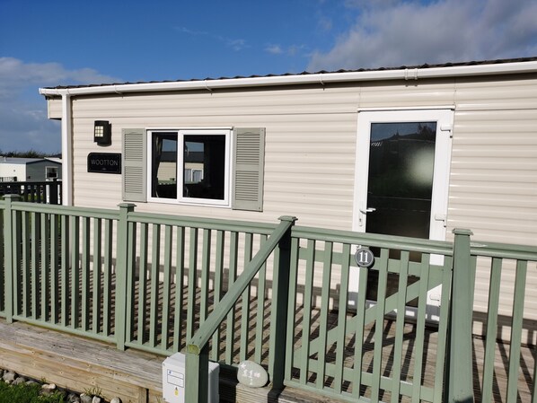 Une maison mobile avec une plaque portant le nom « WOOTTON », une fenêtre avec des volets et une porte portant le numéro « 11 ».