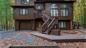 A two-story wooden house with a central staircase, large windows, and a deck surrounded by fallen leaves. - Modern Poconos Game House, Hot Tub, Fire Pit (East Stroudsburg)