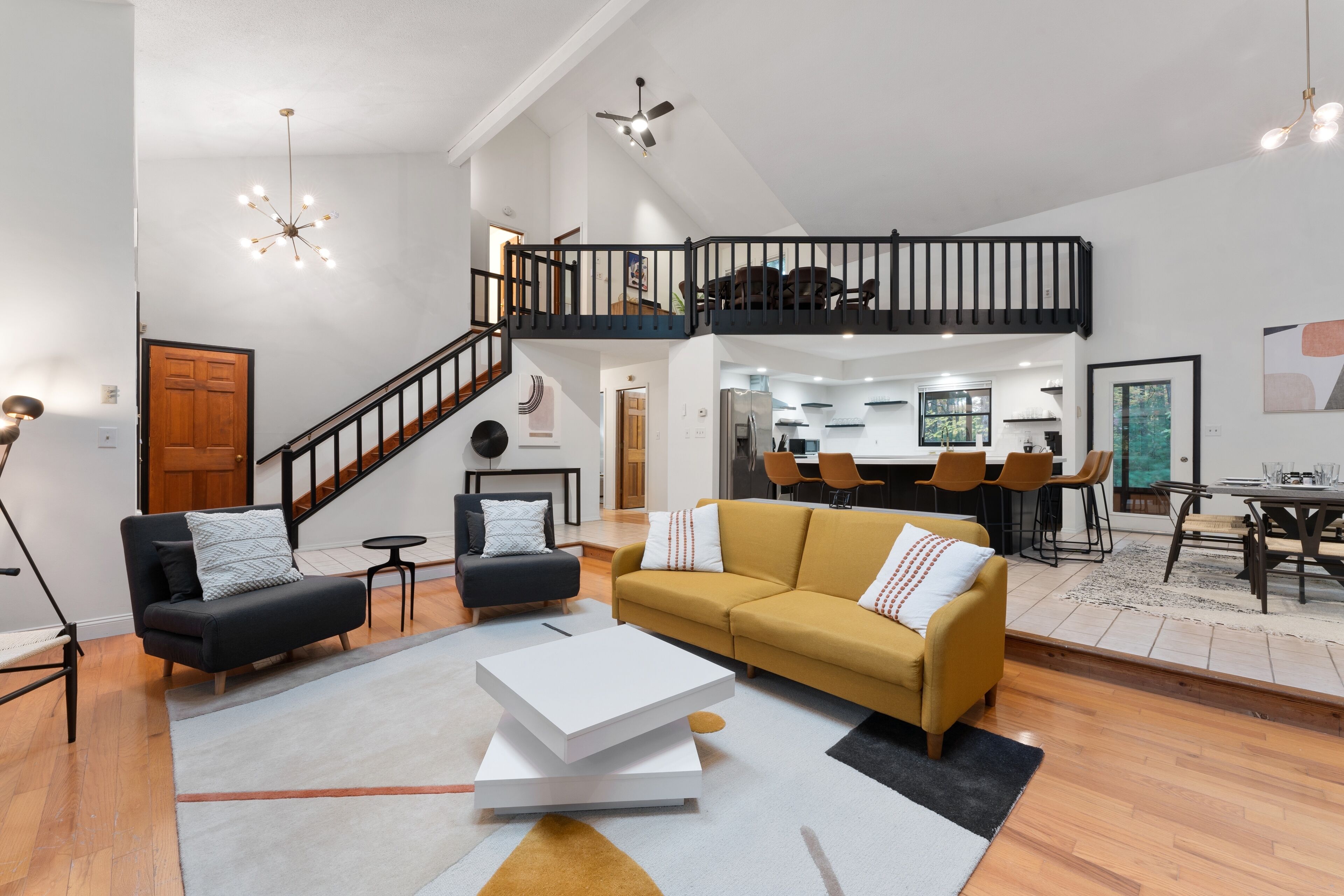 A spacious living area with a high ceiling, a staircase, and a dining area with modern furniture.
