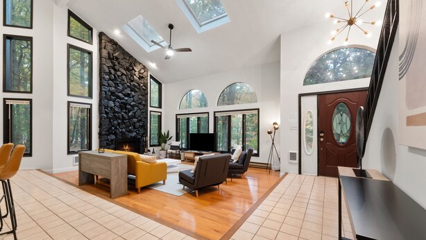 A spacious living room with a stone wall, large windows, and a fireplace. - Modern Poconos Game House, Hot Tub, Fire Pit (East Stroudsburg)