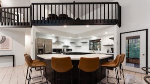 A modern kitchen with a central island, black bar stools, and a staircase leading to an upper level. - Modern Poconos Game House, Hot Tub, Fire Pit (East Stroudsburg)