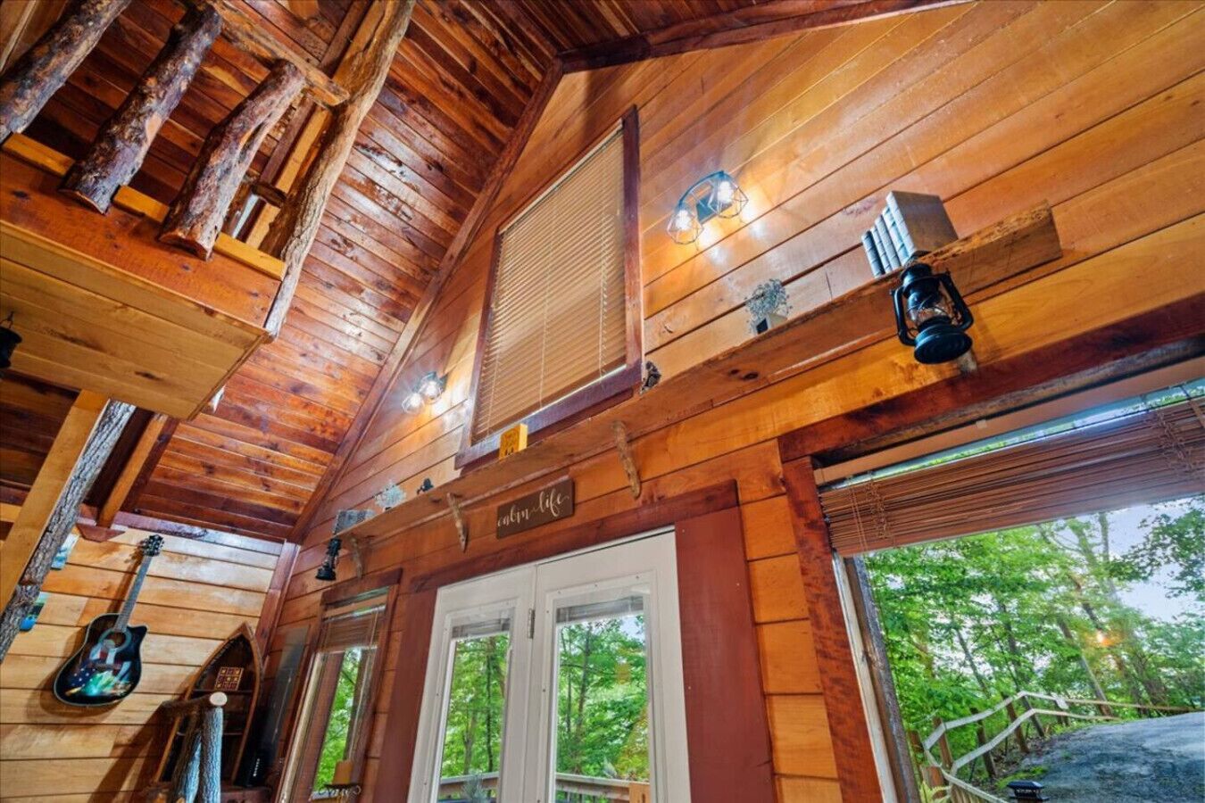 A cabin interior with wooden walls, a sloped ceiling, and a window overlooking greenery.