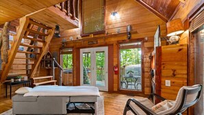 Ein gemütliches Blockhaus-Interieur mit einem Bett, einem Sessel, einer Treppe und Blick ins Freie.