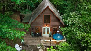 Eine Holzhütte mit Whirlpool auf der Terrasse, umgeben von dichtem Wald.
