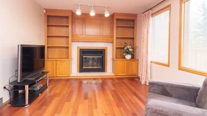 Un salon avec une cheminée, des étagères en bois, un téléviseur et un canapé gris.