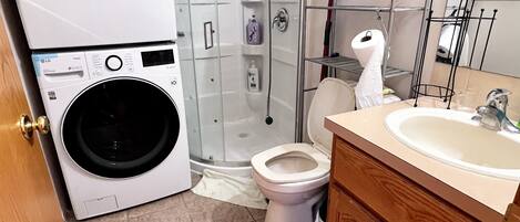 A compact bathroom with a washing machine, a toilet, a shower, and a sink.