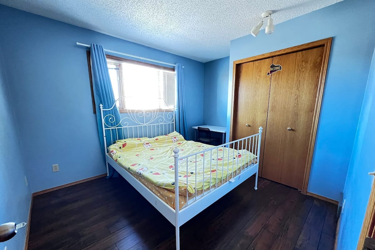 A bedroom with a bed, a desk, and a wardrobe.