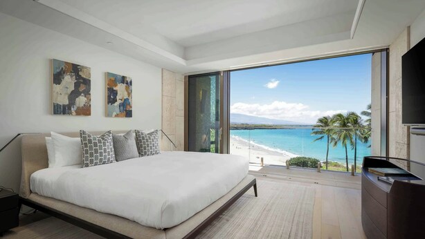 Un dormitorio moderno con una cama grande, una mesita de noche, un televisor de pantalla plana y vistas a la playa y al océano.