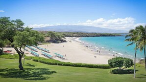 Una playa con agua azul cristalina, una orilla de arena y una cadena montañosa distante.