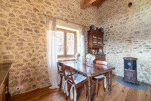 A rustic stone-walled dining area with a wooden table, chairs, and a cabinet.
