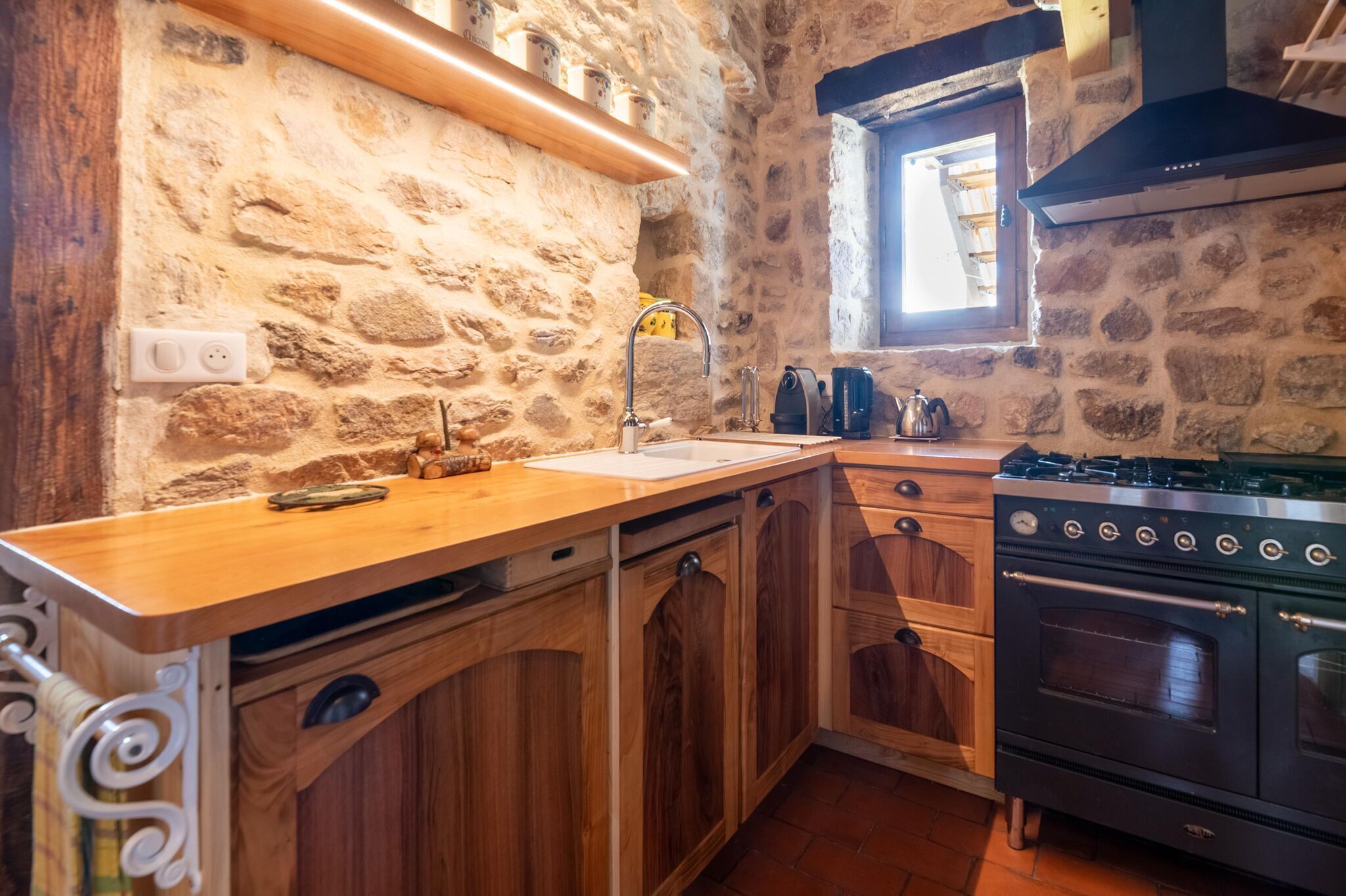 Una cocina con paredes de piedra, armarios de madera, horno empotrado y una ventana.