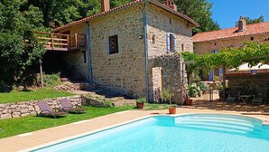 Une maison en pierre avec une piscine, une terrasse en bois et un jardin.