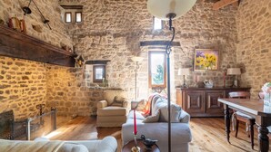 Une pièce rustique aux murs de pierre, avec un plafond en bois, un canapé, une table sur laquelle est posée une bougie rouge et un tableau représentant des tournesols.
