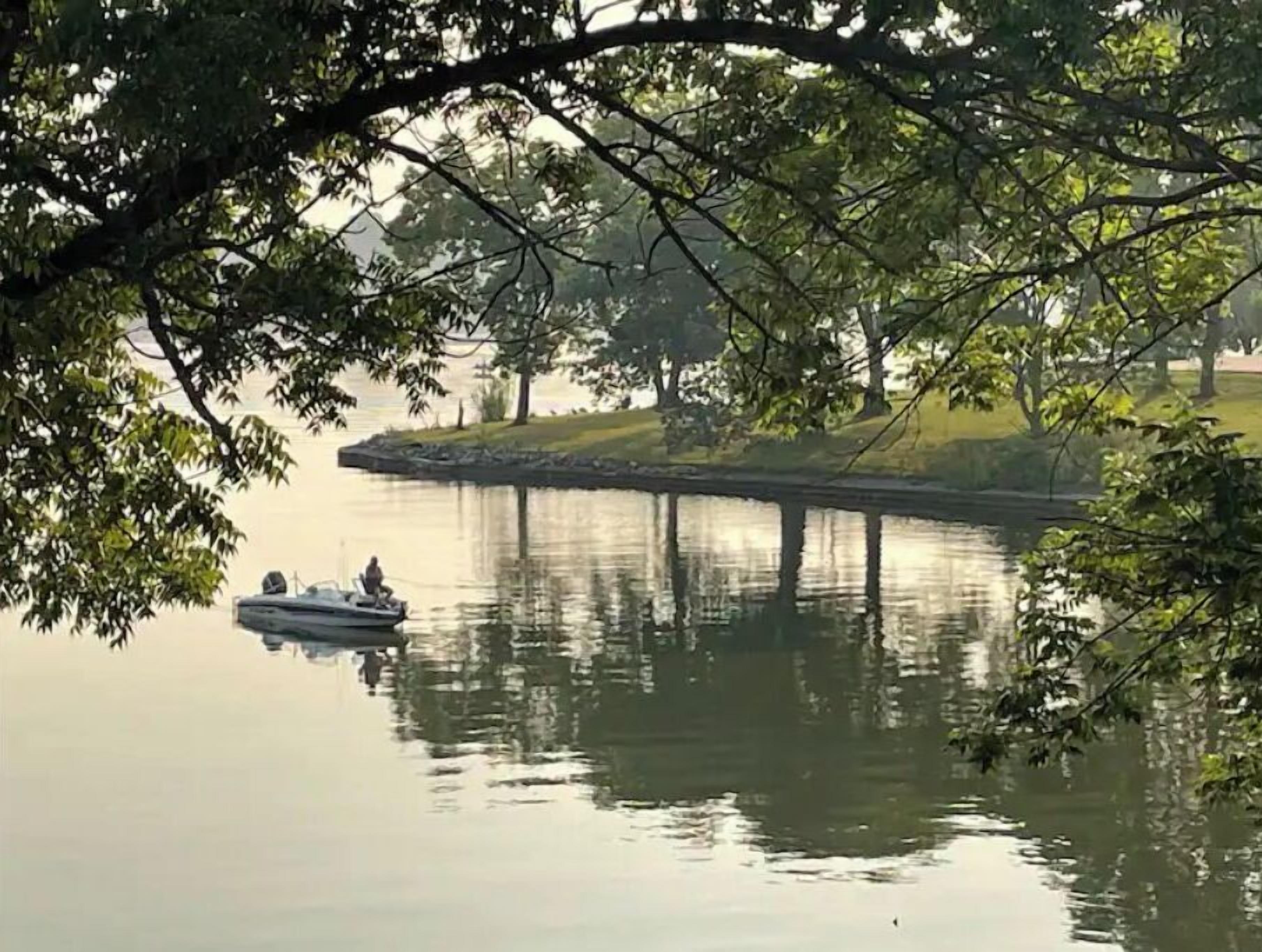 A calm lake with a dock extending into the water, surrounded by trees and grassy areas.