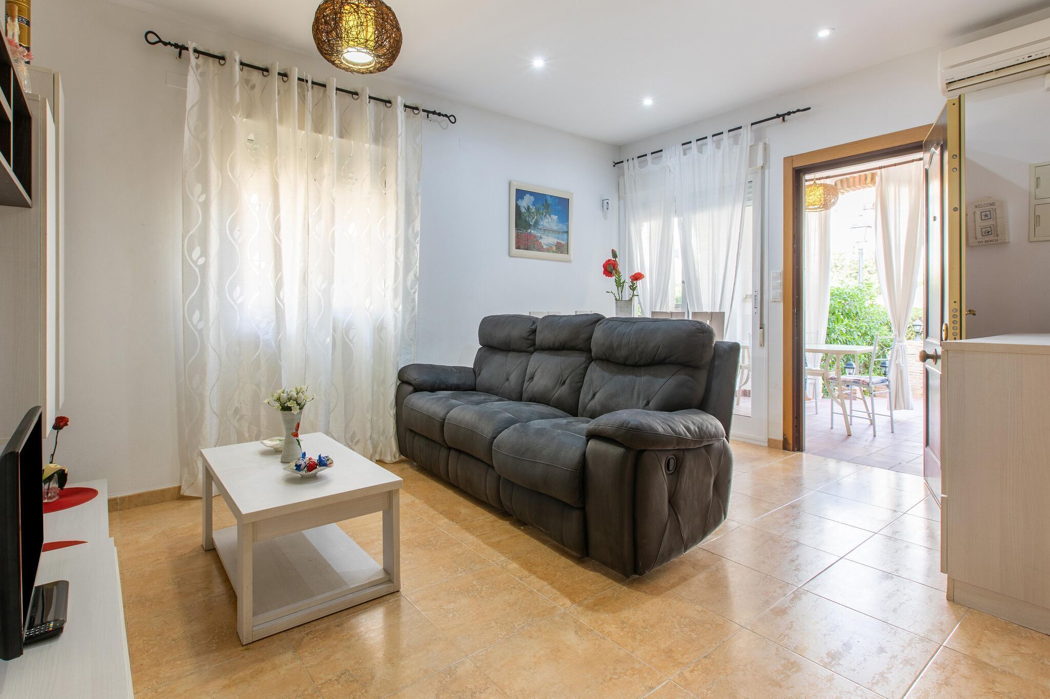 A living room with a grey sofa, a white coffee table, and a TV on a stand.