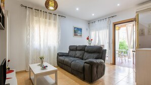 Una sala de estar con un sofá gris, una mesa de centro blanca y un televisor sobre un mueble.