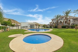 Un área de piscina con una piscina circular, un edificio moderno y un jardín ajardinado con palmeras.