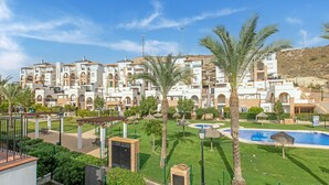 Un hotel con varios pisos, piscina, y un jardín cuidado con palmeras y una fuente.