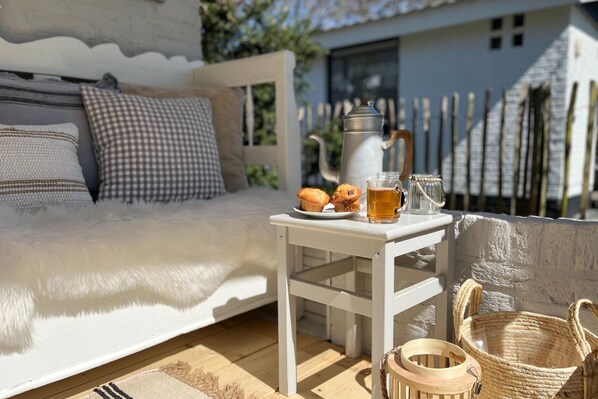 A cozy outdoor seating area with a white table, wicker baskets, and a coffee setup.