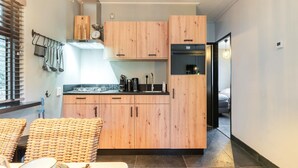Cocina compacta con armarios de madera, horno integrado y comedor con mobiliario de mimbre.